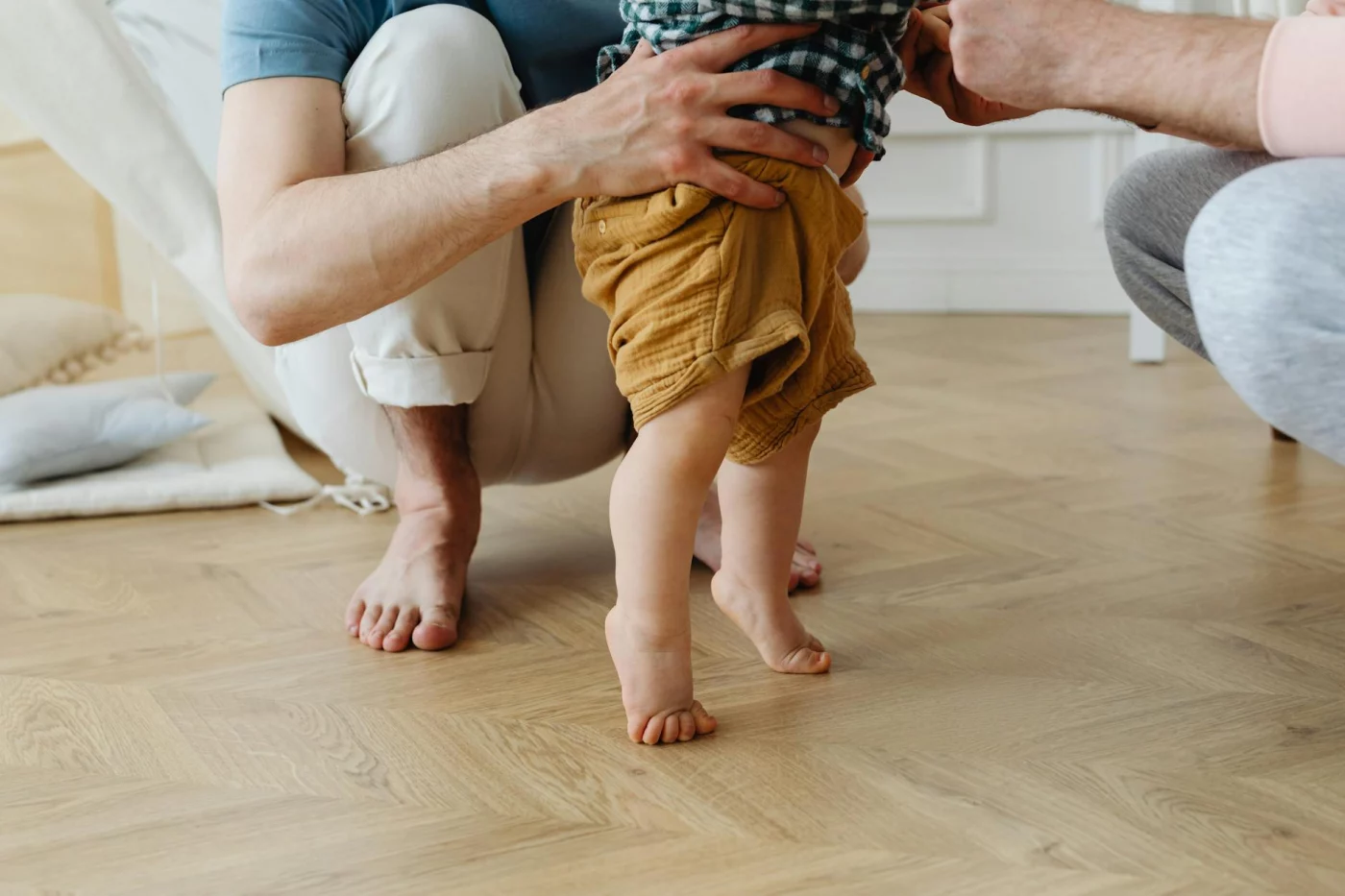 Father helping his baby take first steps at home, showing what are physical development milestones in early childhood