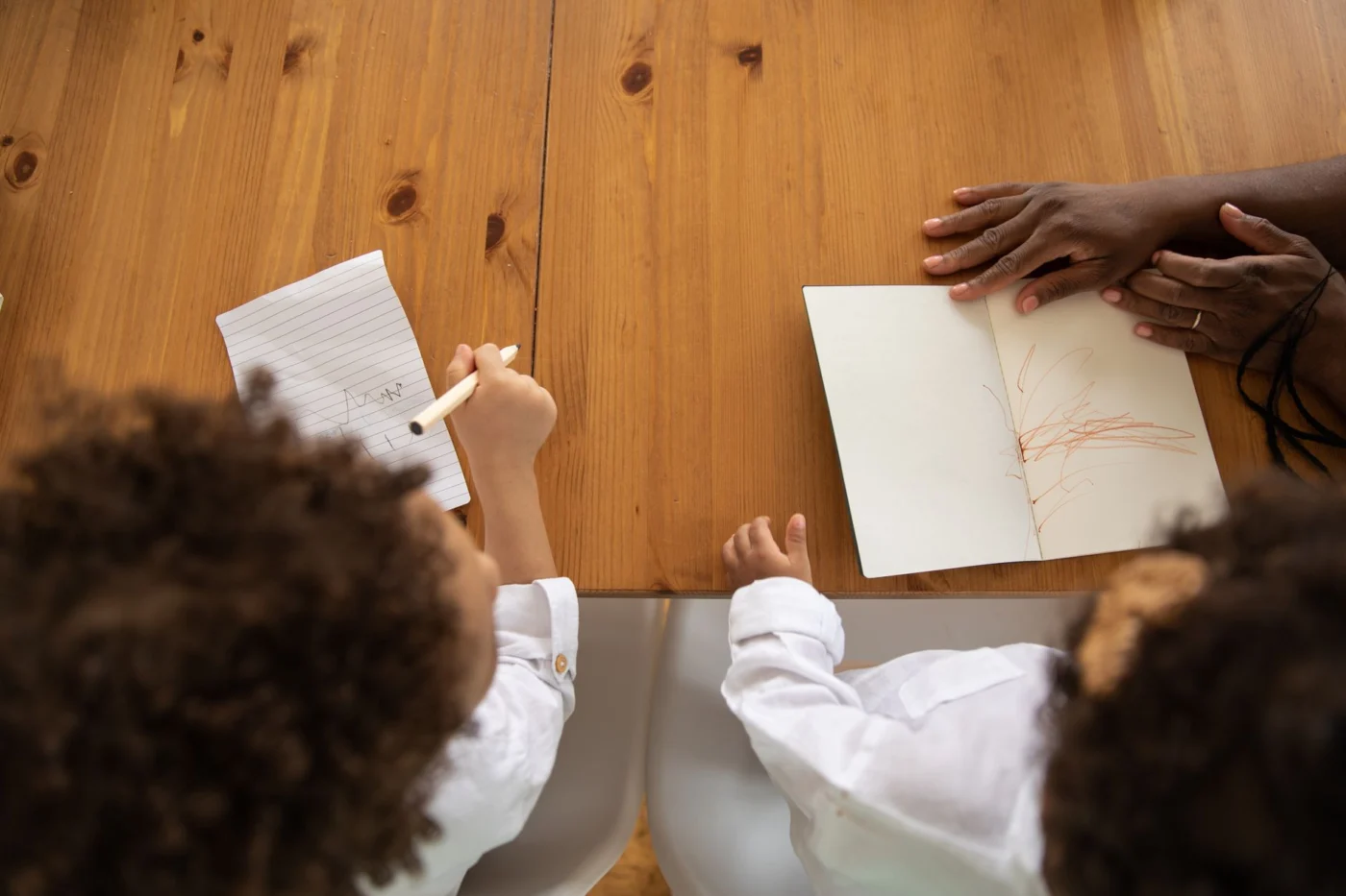 Children drawing at a table while adults review homeschool planning notes
