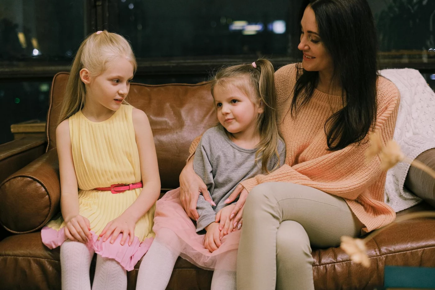 Mother sitting with her two daughters on a sofa, showing how does authoritative parenting work in daily life